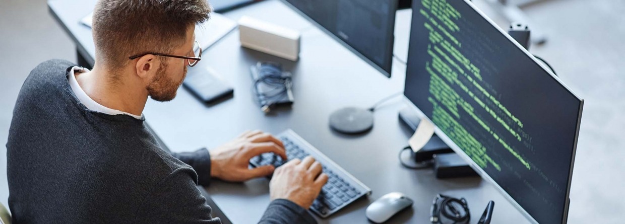 Software ontwikkelaar schrijft code zittend achter een computer en data systeem