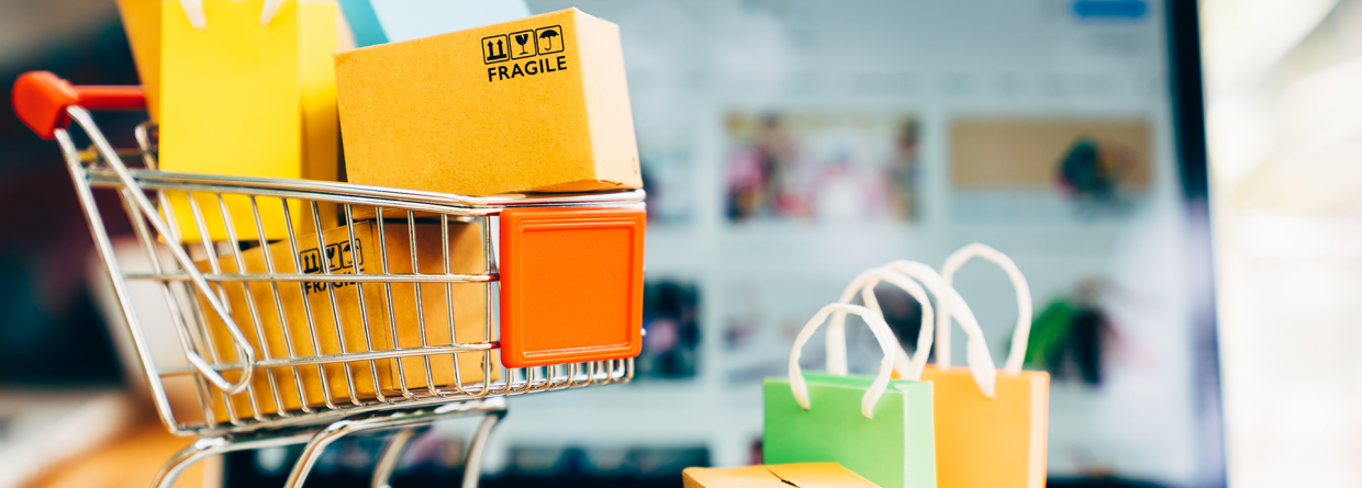 Webshop, online shoppen: laptop met er voor een winkelwagentje met allemaal tasjes erin en ervoor