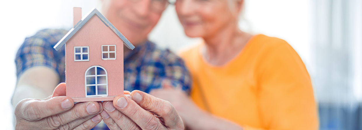 Senioren stel houdt een model huisje vast