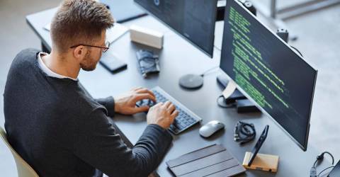 Software ontwikkelaar schrijft code zittend achter een computer en data systeem