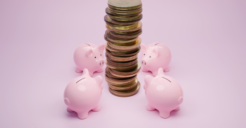 Vier roze spaarvarkens staan om een stapel munten heen met een roze achtergrond